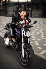 Fototapeta na wymiar Laughing girl in a black jacket sits on a purple motorbike with a red safety helmet