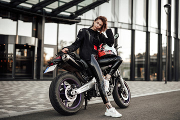 Beautiful young brunette lady in a black motorcycle jacket sits on a purple sport motorbike