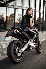 Obraz na płótnie Canvas Beautiful young brunette girl in a black motorcycle jacket sits on a purple sport motorbike
