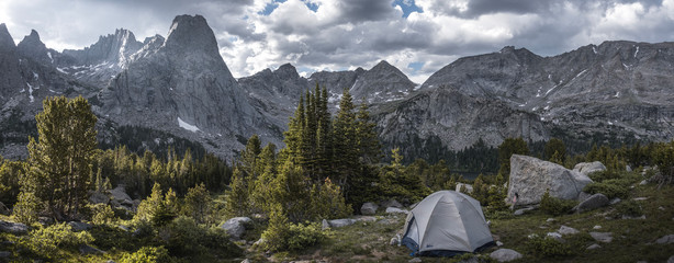 A lone tent in the valley of surrounding mountains. The fading light of day breaks through an...