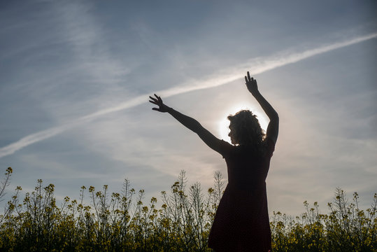 Silhouette woman with arms raised standing amidst oilseed rapes at sunset
