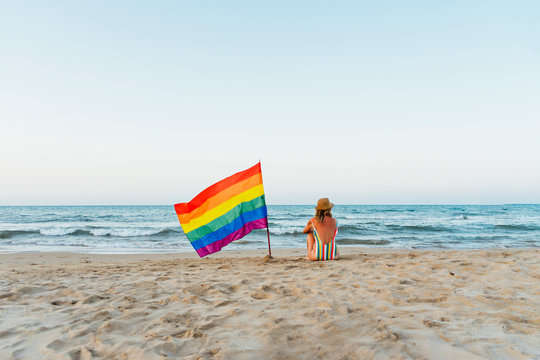 Marure woman sitting on the beach with gay pride flag