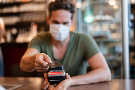 Man with protective mask paying with credit card in restaurant