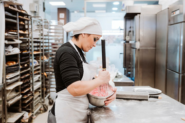 Female baker mixing cake batter in bowl at commercial kitchen