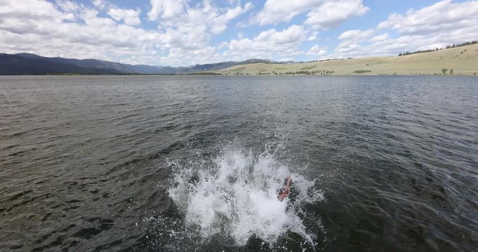 Young Couple Running And Jumping Off Dock Into Lake On Vacation On Hot Summers Day.