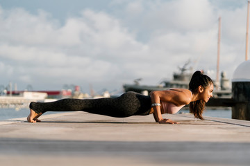 Female athlete practicing four-limbed staff pose on pier at harbor