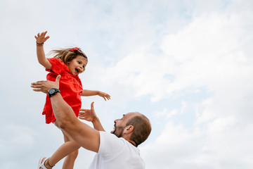 Cheerful father lifting daughter against sky