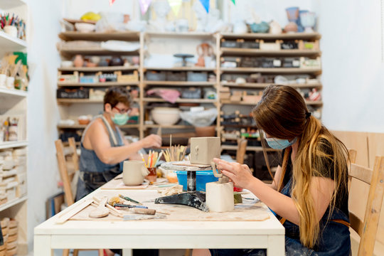 Women wearing masks making ceramics on bench in workshop