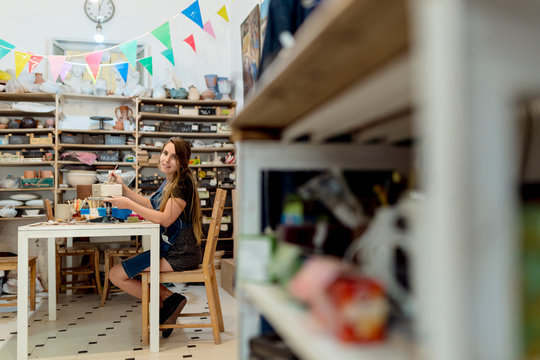 Young woman making pottery on table while sitting in workshop