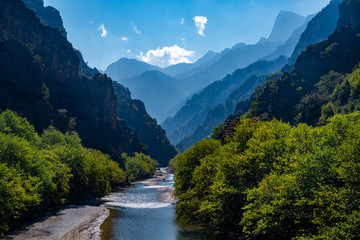 Fototapeta na wymiar Loving landscape with mountains, forest and a river in front located in Greece. Beautiful scenery ideal for wallpaper taken from Greek mythology.