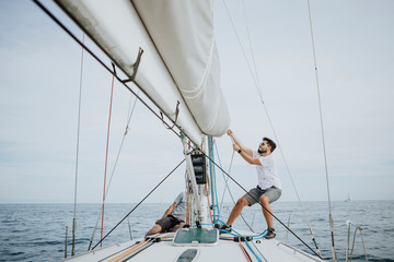 Sailor maneuvering setting the mainsail in sailboat against sky