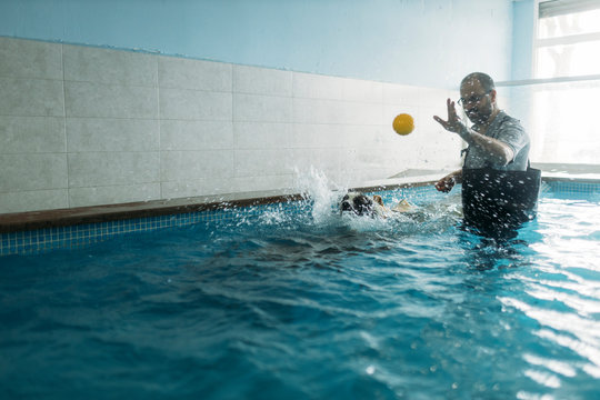 Male physiotherapist throwing ball towards Border Collie in swimming pool
