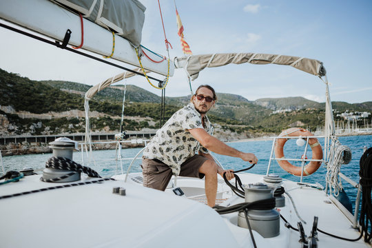 Male sailor maneuvering with winch in sailboat against sky
