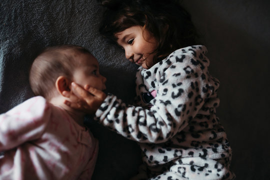 Girl touching baby sister's cheeks while lying on bed at hone