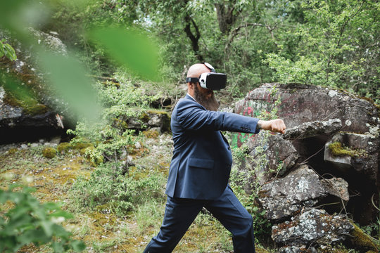 Businessman looking through virtual reality simulator practicing martial arts in forest