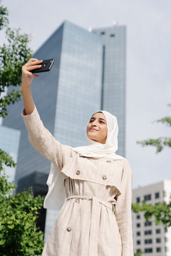 Muslim teenage girl taking selfie through smart phone in city during sunny day