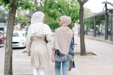 Muslim sisters talking while walking on sidewalk in city