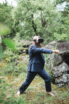 Businessman looking through virtual reality simulator practicing martial arts against trees in forest