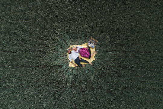Drone shot of mature couple lying on blanket amidst green cornfield