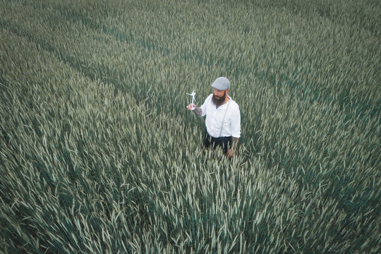Drone shot of man holding small windmill while standing amidst cornfield