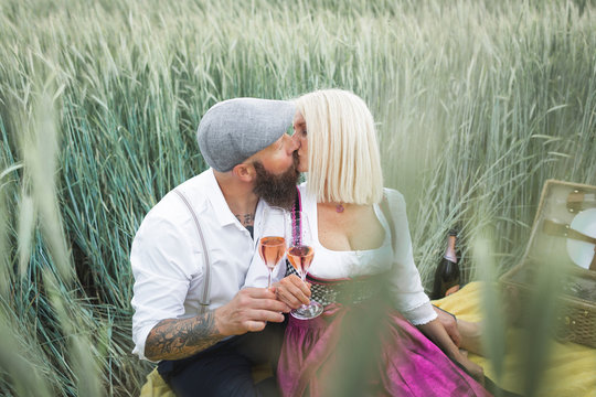 Couple holding champagne glasses kissing while sitting amidst plants on land