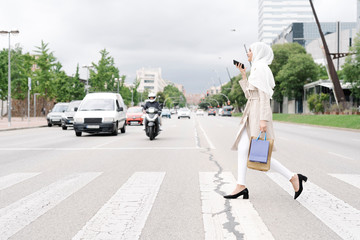 Muslim teenage girl talking through smart phone while crossing road in city