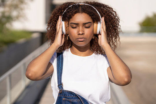 Close-up of afro young woman listening music through headphones while standing in city