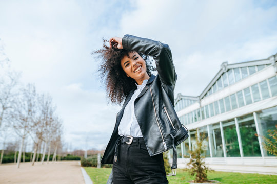 Cheerful Young Afro Woman With Hand In Hair While Standing Against Sky