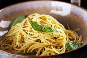 Plate of delicious spaghetti pesto garnished with parmesan cheese and basil on rustic dark background