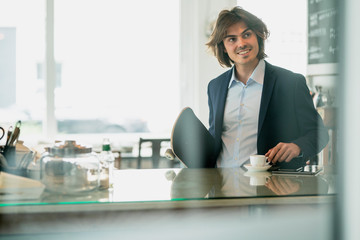 Smiling businessman with skateboard holding coffee on counter in cafe
