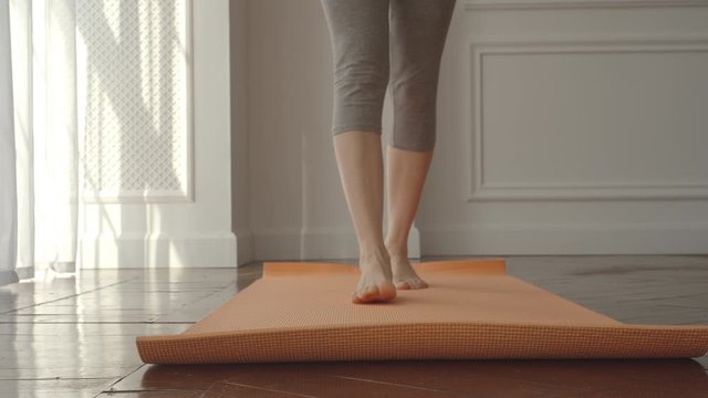 Young sport woman opens a mat getting started yoga at home