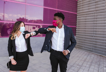 Business people wearing masks giving elbow bump while standing against modern building