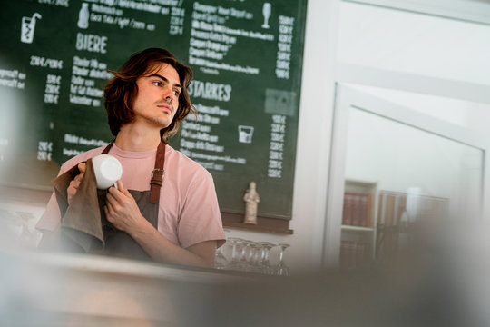 Barista cleaning coffee cup looking away while standing in cafe
