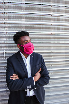 Thoughtful businessman wearing mask with arms crossed standing against wall in city