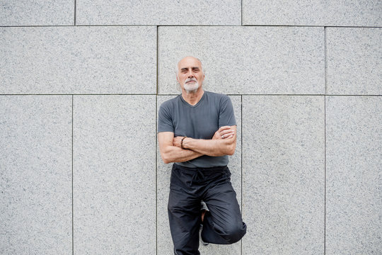 Confident senior man with arms crossed standing against wall in city