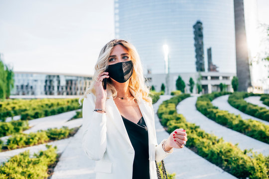 Female entrepreneur wearing face mask talking over smart phone while standing in city