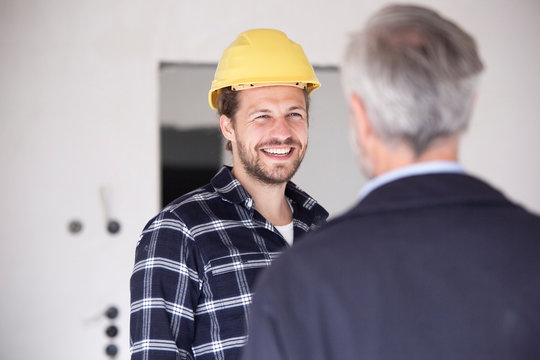 Smiling construction worker wearing hardhat talking with architect in constructing home