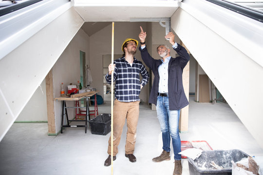 Architect and construction worker discussing about frame in renovating house seen through window