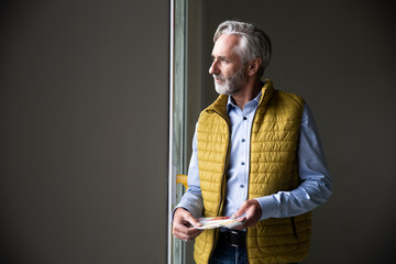 Thoughtful male architect wearing jacket looking through window in constructing home