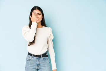 Young indian woman isolated on blue background having fun covering half of face with palm.