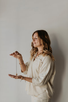 Mid adult woman holding pendulum meditating while standing against white wall