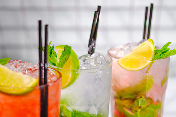 Three refreshing summer cocktails in glasses with tubes on the bar rack.