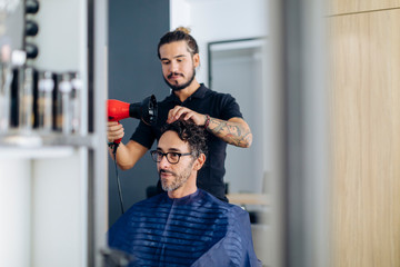 Hairdresser blow drying man's hair at salon