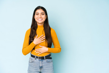 Young indian woman isolated on blue background laughs happily and has fun keeping hands on stomach.