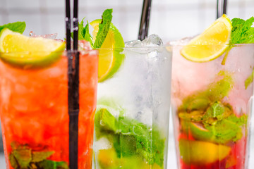 Three refreshing summer cocktails in glasses with tubes on the bar rack.