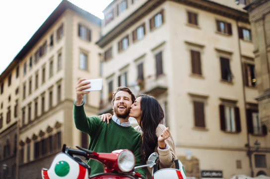 Man taking selfie with girlfriend kissing him on cheeks in Florence city, Italy
