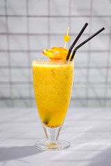 A glass of tasty fresh fruit yellow cocktail with a tube.
