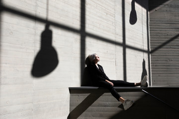 Businesswoman wearing elegant suit sitting on retaining wall with sunlight and shadow in background