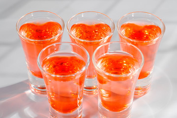 Red alcoholic shot drinks in glasses in a row on the bar count.