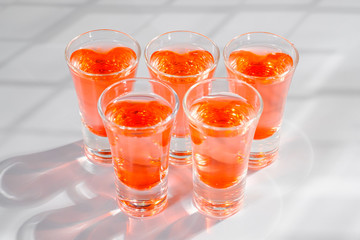 Red alcoholic shot drinks in glasses in a row on the bar count.